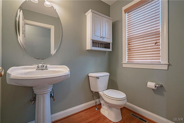 half bath featuring toilet, wood finished floors, visible vents, baseboards, and a wealth of natural light