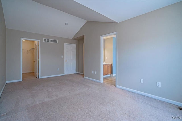 unfurnished bedroom with baseboards, visible vents, light colored carpet, a spacious closet, and vaulted ceiling