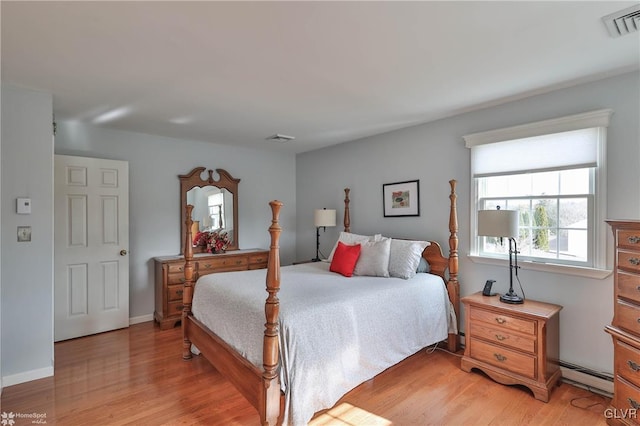 bedroom with light wood finished floors, baseboard heating, visible vents, and baseboards