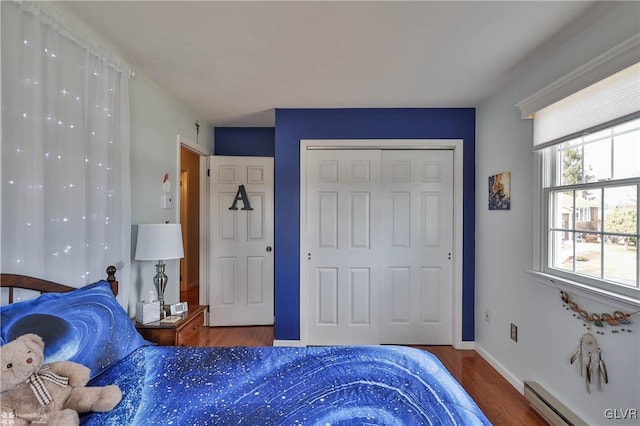 bedroom with a baseboard heating unit, a closet, wood finished floors, and baseboards