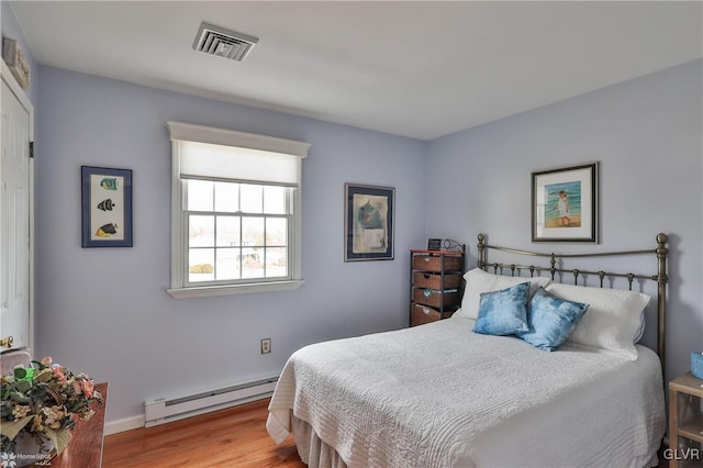 bedroom featuring a baseboard heating unit, visible vents, baseboards, and wood finished floors