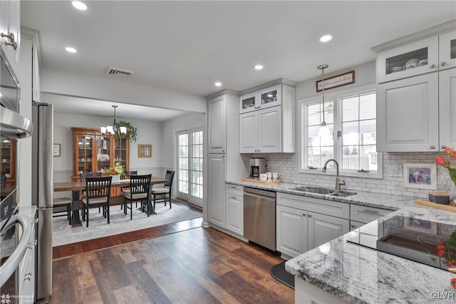 kitchen with stainless steel appliances, a sink, dark wood-style floors, glass insert cabinets, and pendant lighting