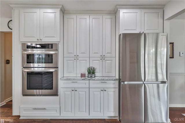 kitchen with light stone counters, appliances with stainless steel finishes, dark wood-type flooring, white cabinets, and baseboards