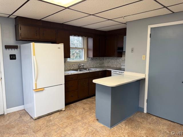 kitchen featuring dark brown cabinetry, light countertops, a sink, and freestanding refrigerator