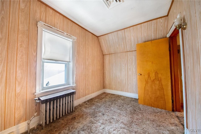 spare room featuring carpet floors, visible vents, vaulted ceiling, wood walls, and baseboards