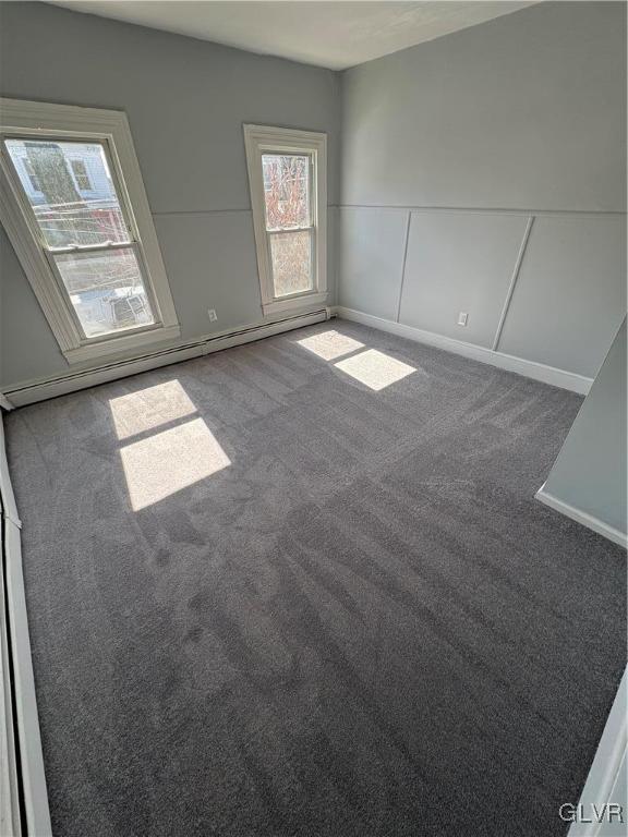 carpeted empty room with baseboard heating, a decorative wall, and wainscoting