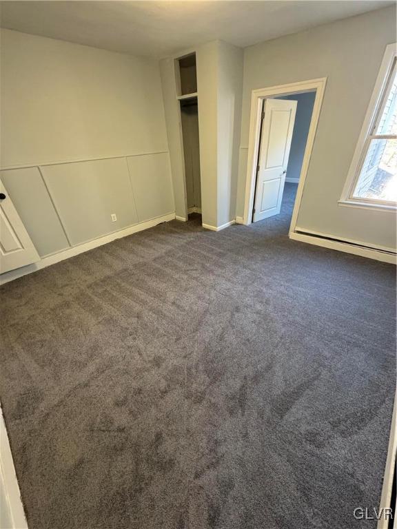 unfurnished bedroom featuring a baseboard radiator, a closet, a decorative wall, and dark colored carpet