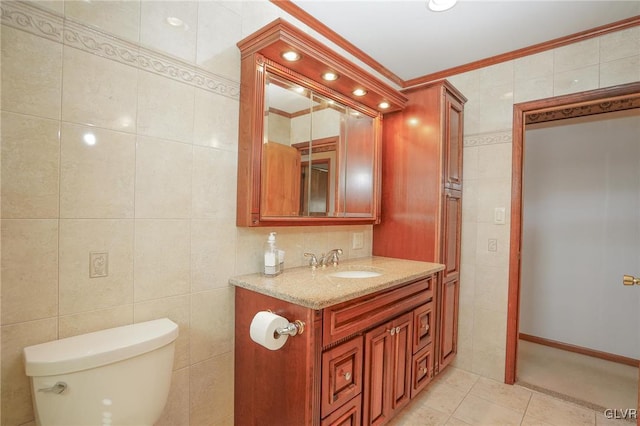 half bath with toilet, vanity, tile walls, tile patterned floors, and crown molding