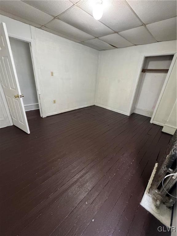 unfurnished bedroom featuring a paneled ceiling, baseboards, and dark wood finished floors