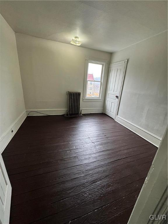 empty room with dark wood-style floors, baseboards, and radiator