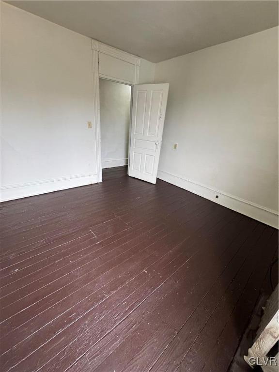 empty room featuring baseboards and dark wood-type flooring