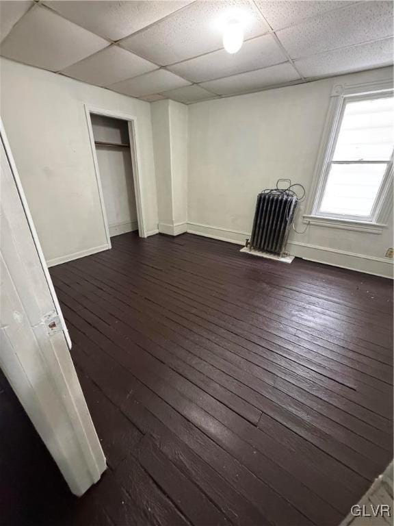 interior space featuring a paneled ceiling, baseboards, dark wood finished floors, and a closet