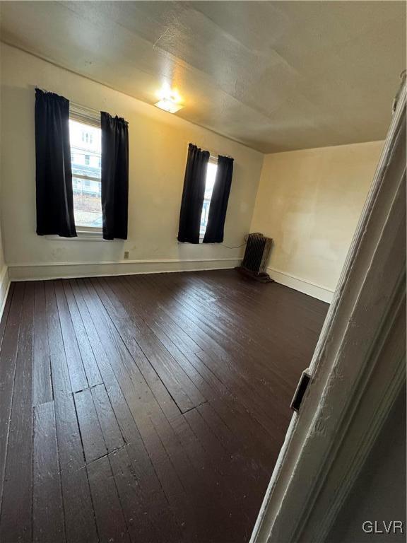 spare room featuring dark wood-type flooring, plenty of natural light, and baseboards