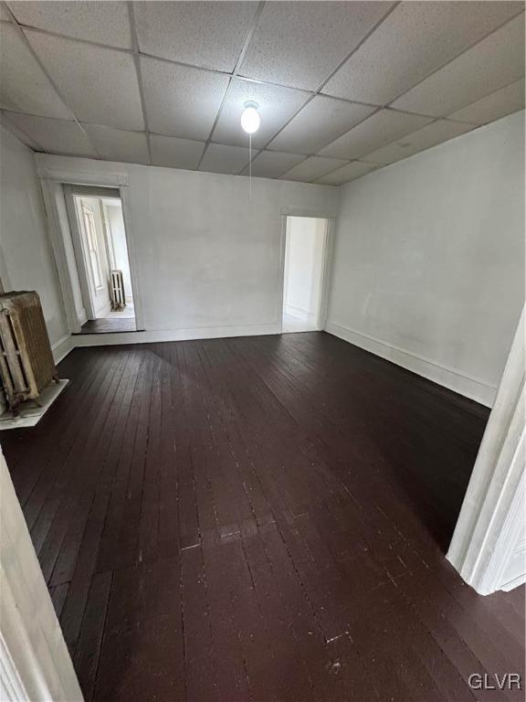 unfurnished room with a drop ceiling, dark wood finished floors, and baseboards