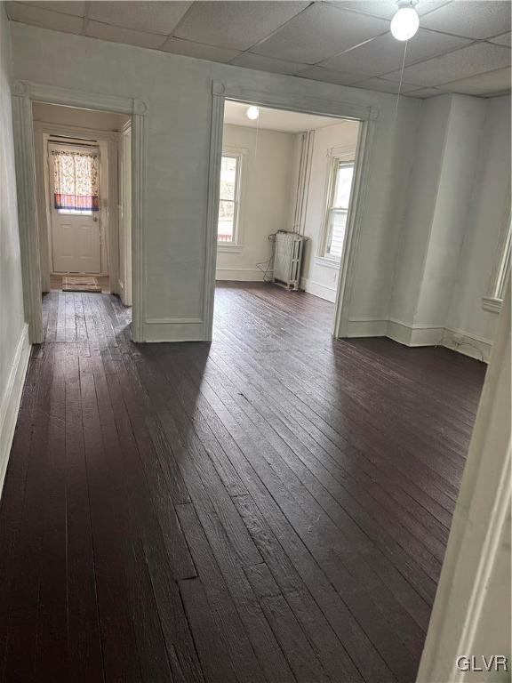 unfurnished room featuring dark wood-style floors, baseboards, a paneled ceiling, and radiator