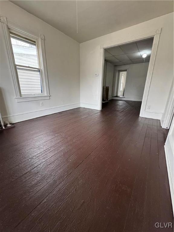 empty room featuring dark wood-style flooring, a drop ceiling, and baseboards