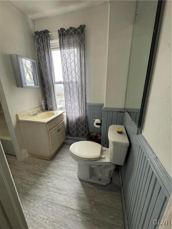 half bath with wainscoting, vanity, and toilet