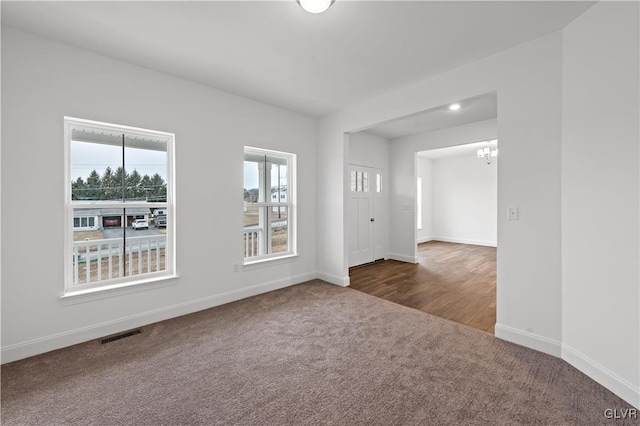 carpeted empty room featuring an inviting chandelier, visible vents, and baseboards