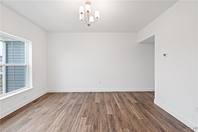 spare room with a chandelier, wood finished floors, visible vents, and baseboards