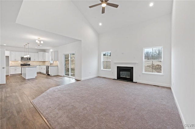 unfurnished living room with baseboards, a fireplace with flush hearth, ceiling fan, high vaulted ceiling, and a sink