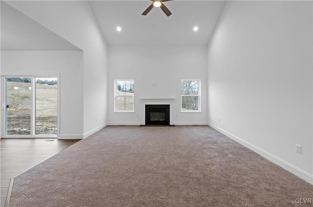 unfurnished living room with baseboards, a ceiling fan, a fireplace with flush hearth, carpet floors, and high vaulted ceiling