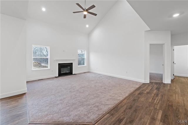 unfurnished living room with ceiling fan, high vaulted ceiling, a fireplace with flush hearth, and baseboards