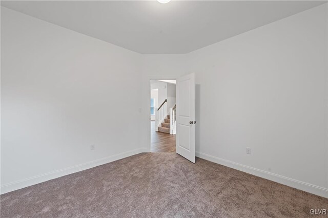 carpeted empty room with stairs and baseboards