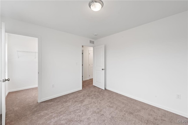 unfurnished bedroom featuring carpet floors, visible vents, baseboards, a spacious closet, and a closet