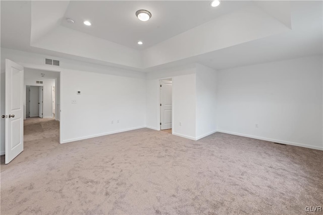 carpeted empty room with a tray ceiling, visible vents, baseboards, and recessed lighting