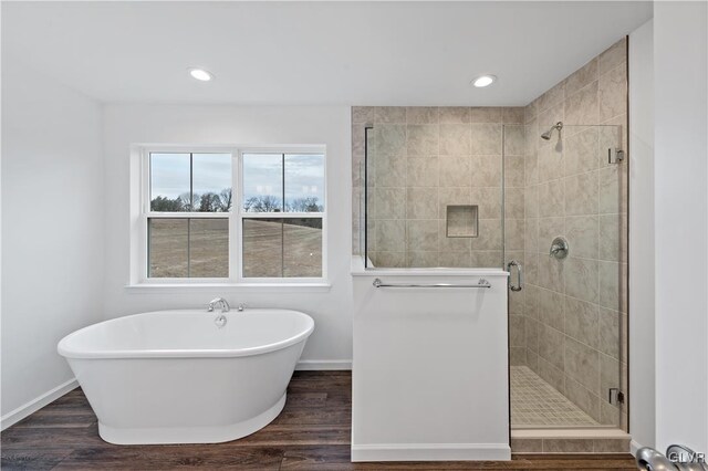 full bath featuring a stall shower, a soaking tub, wood finished floors, and baseboards