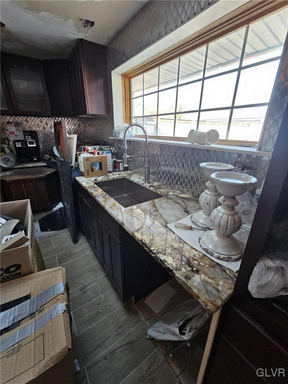 kitchen featuring light stone countertops, light wood-style flooring, decorative backsplash, and a sink