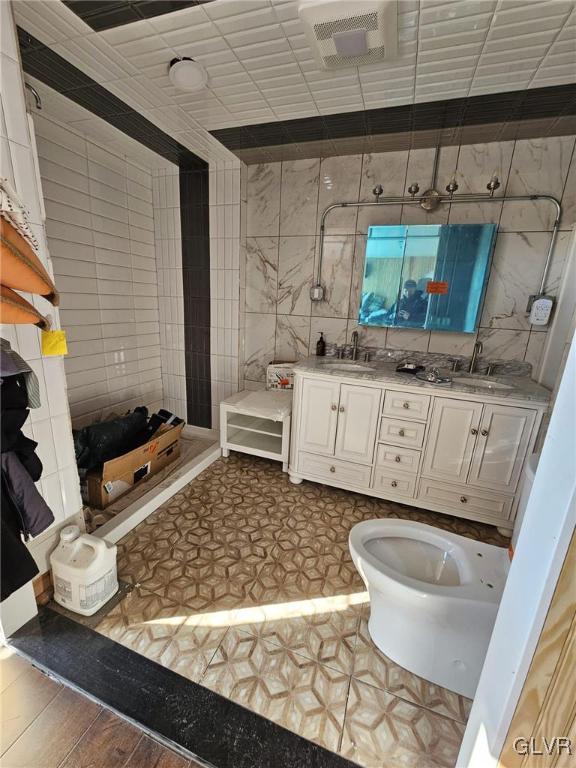 bathroom featuring wood finished floors, a sink, tile walls, and double vanity