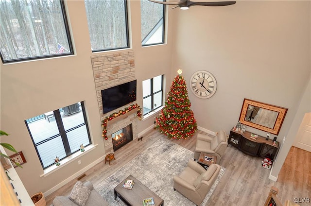 living room with baseboards, a stone fireplace, a towering ceiling, and wood finished floors