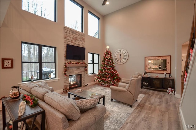 living area with light wood-style floors, a high ceiling, a stone fireplace, and baseboards