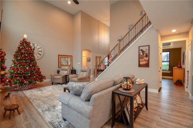 living room with arched walkways, light wood-style flooring, a high ceiling, baseboards, and stairs