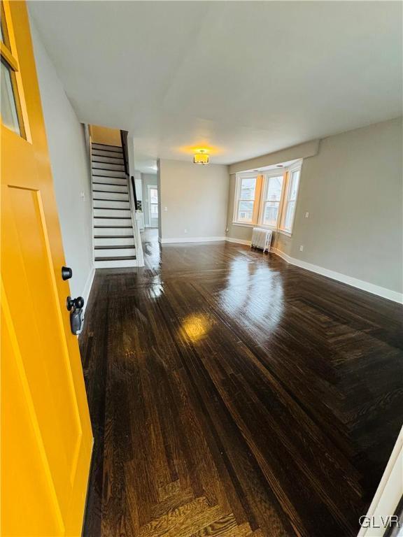 unfurnished living room featuring radiator, wood finished floors, baseboards, and stairs