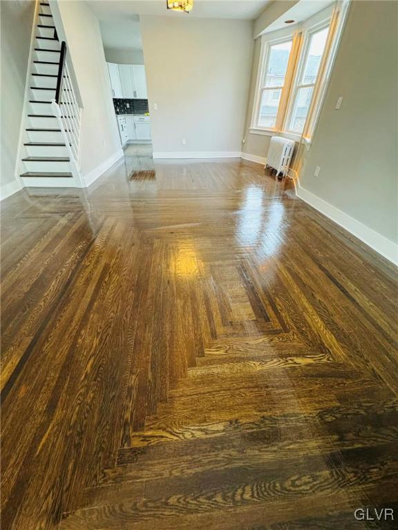 unfurnished living room featuring a wall mounted air conditioner, baseboards, and stairs