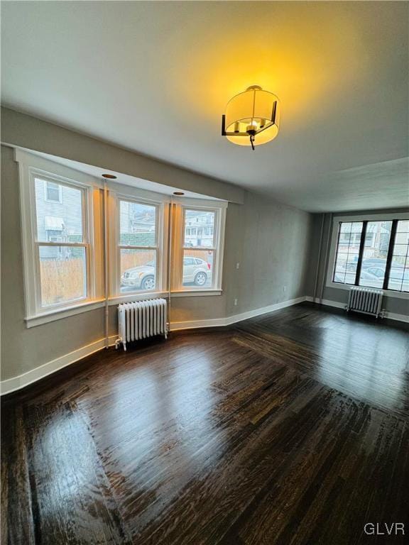 empty room featuring radiator, dark wood-style floors, and baseboards