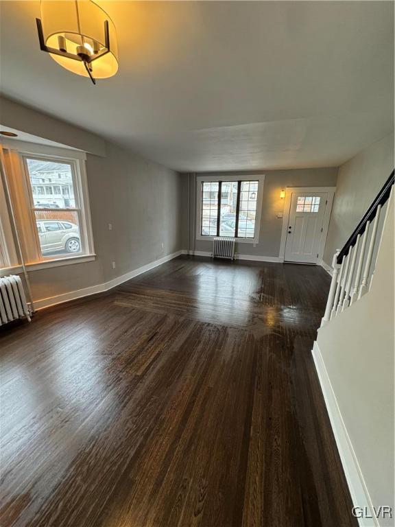 unfurnished living room featuring baseboards, radiator heating unit, stairway, and dark wood-style flooring