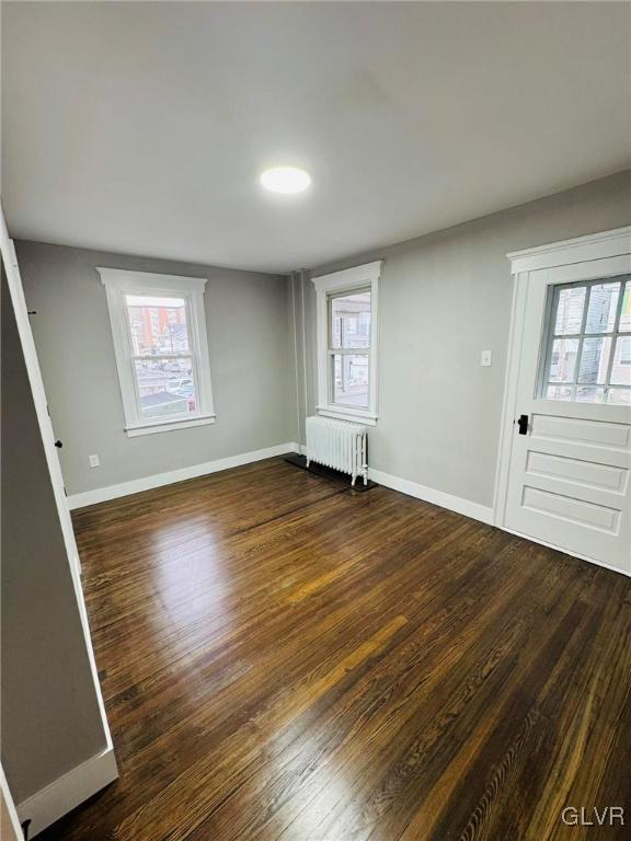 unfurnished room featuring baseboards, dark wood-type flooring, and radiator