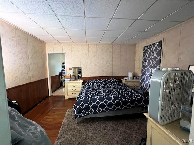 bedroom with a wainscoted wall, a drop ceiling, and dark wood-style flooring