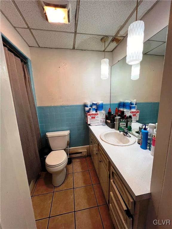 full bath with a drop ceiling, vanity, toilet, and tile patterned floors