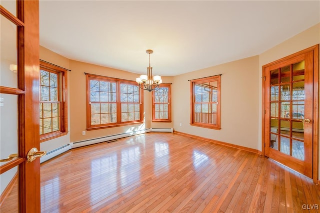 spare room featuring a notable chandelier, a baseboard heating unit, baseboards, and light wood-style floors