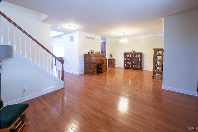 living area with hardwood / wood-style flooring, visible vents, ornamental molding, wainscoting, and an inviting chandelier