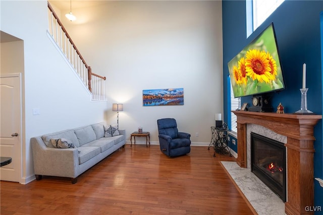 living area with a fireplace, wood finished floors, a towering ceiling, and baseboards