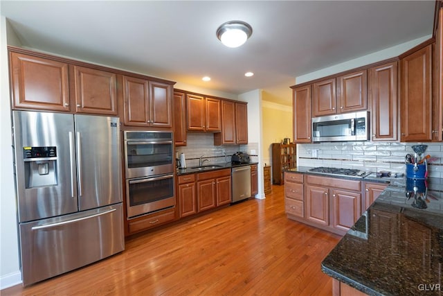 kitchen with light wood finished floors, stainless steel appliances, tasteful backsplash, a sink, and dark stone counters