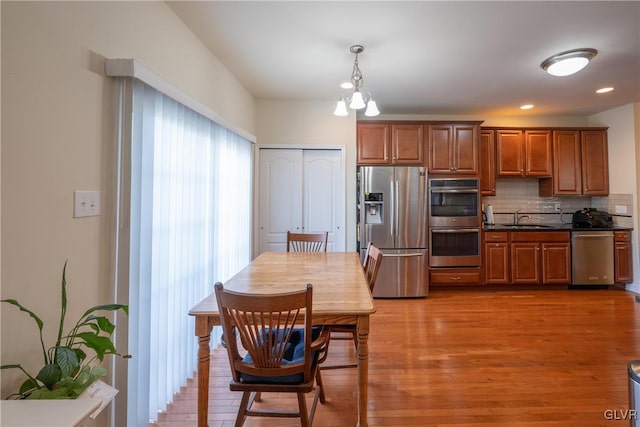 kitchen featuring brown cabinetry, dark countertops, appliances with stainless steel finishes, a sink, and backsplash