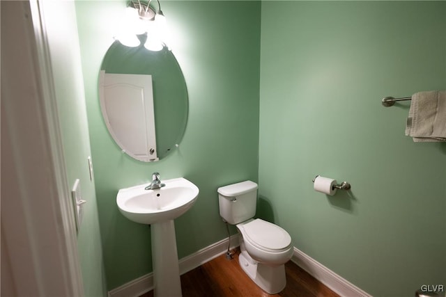 half bathroom with baseboards, a sink, toilet, and wood finished floors