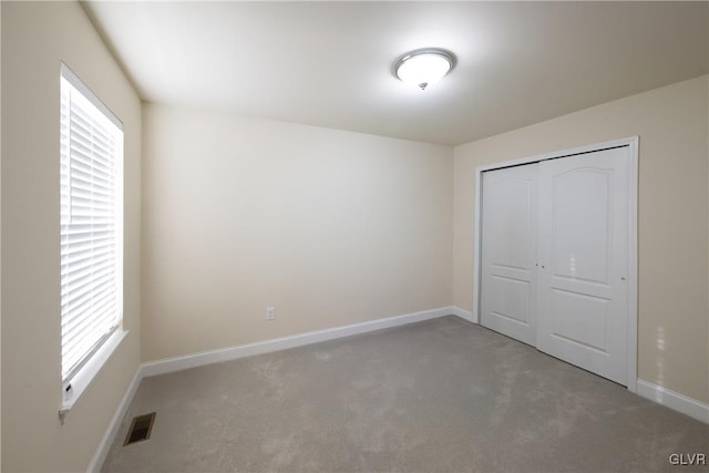 unfurnished bedroom featuring carpet, multiple windows, visible vents, and baseboards