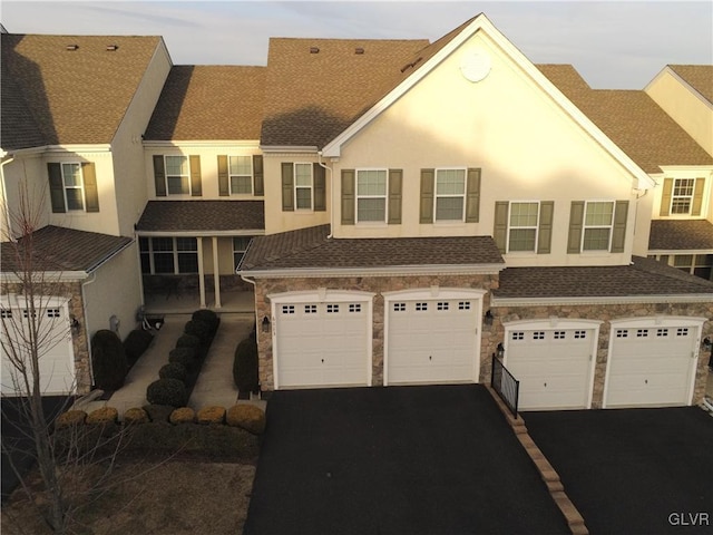 view of property featuring stone siding, an attached garage, driveway, and stucco siding